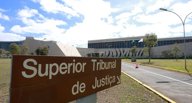 Placa do Superior Tribunal de Justiça diante da sede do tribunal, em Brasília, sob céu azul com nuvens