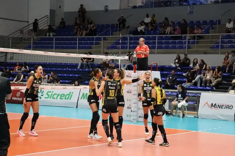 Jogadoras do Praia Clube, de uniforme preto e amarelo, comemoram um ponto em quadra, com o árbitro ao fundo