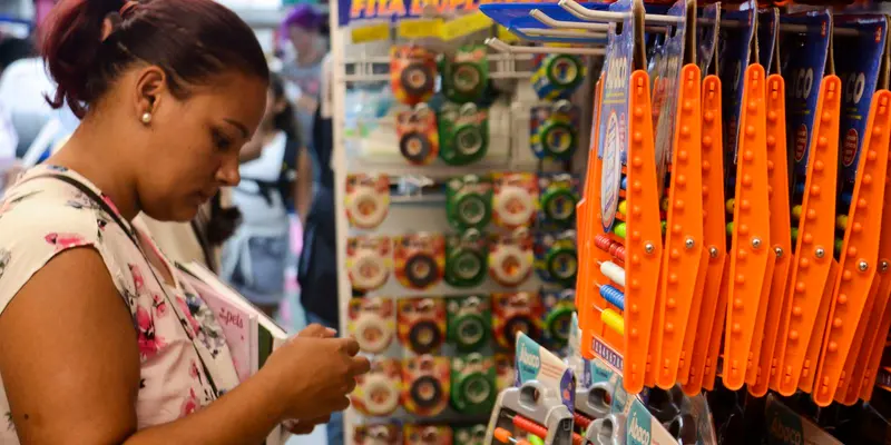 Consumidora escolhe produtos em loja de material escolar com canetas e fitas expostas